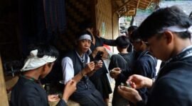 Seorang nenek di pedesaan Sunda sedang meracik ramuan herbal menggunakan tumbuk tradisional, menunjukkan kearifan turun-temurun dalam mengolah tanaman obat alami. Berbagai jenis dedaunan dan akar terlihat di sekelilingnya, siap diolah menjadi obat untuk menjaga kesehatan.
