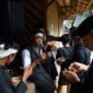 Seorang nenek di pedesaan Sunda sedang meracik ramuan herbal menggunakan tumbuk tradisional, menunjukkan kearifan turun-temurun dalam mengolah tanaman obat alami. Berbagai jenis dedaunan dan akar terlihat di sekelilingnya, siap diolah menjadi obat untuk menjaga kesehatan.