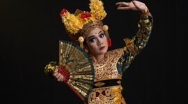 Seorang penari Jaipong dengan kostum warna-warni yang cerah sedang menampilkan gerakan lincah penuh ekspresi, diiringi alunan musik gamelan khas Sunda. Tarian ini melambangkan semangat dan kekayaan budaya Indonesia yang terus lestari.