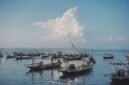 Pemandangan udara pantai Pangandaran saat matahari terbenam menampilkan jajaran perahu nelayan tradisional yang berlabuh, menciptakan siluet indah di ufuk barat. Sebuah gambaran sempurna keindahan pesisir selatan Jawa Barat yang memukau.