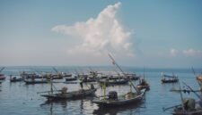 Pemandangan udara pantai Pangandaran saat matahari terbenam menampilkan jajaran perahu nelayan tradisional yang berlabuh, menciptakan siluet indah di ufuk barat. Sebuah gambaran sempurna keindahan pesisir selatan Jawa Barat yang memukau.