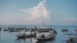 Pemandangan udara pantai Pangandaran saat matahari terbenam menampilkan jajaran perahu nelayan tradisional yang berlabuh, menciptakan siluet indah di ufuk barat. Sebuah gambaran sempurna keindahan pesisir selatan Jawa Barat yang memukau.
