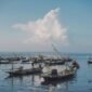 Pemandangan udara pantai Pangandaran saat matahari terbenam menampilkan jajaran perahu nelayan tradisional yang berlabuh, menciptakan siluet indah di ufuk barat. Sebuah gambaran sempurna keindahan pesisir selatan Jawa Barat yang memukau.