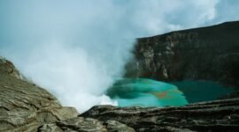 Pemandangan udara Kawah Putih Ciwidey yang menakjubkan, menunjukkan danau kawah berwarna putih kehijauan dikelilingi lanskap pegunungan yang asri. Visual ini memperlihatkan keunikan geologis dan keindahan alam yang menjadi daya tarik utama destinasi wisata populer tersebut.