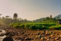 Pemandangan Sungai Citarum pada tahun 2026 yang menunjukkan air jernih dengan vegetasi hijau di tepian, mencerminkan keberhasilan upaya restorasi lingkungan yang telah dilakukan. Perahu-perahu tradisional terlihat melintas, menandakan kehidupan dan aktivitas masyarakat yang kembali pulih di sepanjang aliran sungai ini.