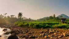Pemandangan Sungai Citarum pada tahun 2026 yang menunjukkan air jernih dengan vegetasi hijau di tepian, mencerminkan keberhasilan upaya restorasi lingkungan yang telah dilakukan. Perahu-perahu tradisional terlihat melintas, menandakan kehidupan dan aktivitas masyarakat yang kembali pulih di sepanjang aliran sungai ini.