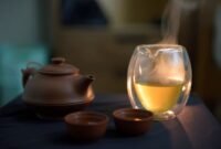 Secangkir teh hijau hangat mengepulkan uap, siap dinikmati untuk memulai hari dengan penuh energi dan manfaat kesehatan. Daun teh hijau segar terlihat di latar belakang, melambangkan kealamian dan kekayaan nutrisi minuman ini.