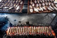 Pemandangan otentik penjual surabi yang tengah membakar adonan di atas tungku arang tradisional, menunjukkan proses pembuatan yang menjaga keaslian rasa dan aroma khasnya. Asap tipis yang mengepul menambah nuansa hangat dari penganan legendaris khas Jawa Barat ini.