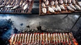 Pemandangan otentik penjual surabi yang tengah membakar adonan di atas tungku arang tradisional, menunjukkan proses pembuatan yang menjaga keaslian rasa dan aroma khasnya. Asap tipis yang mengepul menambah nuansa hangat dari penganan legendaris khas Jawa Barat ini.