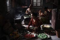 Seorang penjual sedang membuat surabi di atas tungku arang tradisional, menunjukkan proses otentik yang menjaga cita rasa khas jajanan legendaris ini. Asap tipis mengepul dari cetakan, menambah daya tarik visual dari kuliner khas Bandung yang selalu dicari ini.
