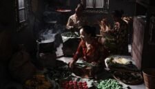 Seorang penjual sedang membuat surabi di atas tungku arang tradisional, menunjukkan proses otentik yang menjaga cita rasa khas jajanan legendaris ini. Asap tipis mengepul dari cetakan, menambah daya tarik visual dari kuliner khas Bandung yang selalu dicari ini.