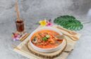Seporsi seblak kuah pedas mengepul yang menggoda selera, dengan berbagai topping melimpah seperti bakso, sosis, dan ceker ayam, siap dinikmati. Hidangan ini memancarkan warna merah merona dari cabai dan aroma khas kencur yang menggugah selera para pencinta makanan pedas.