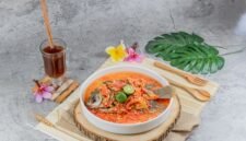 Seporsi seblak kuah pedas mengepul yang menggoda selera, dengan berbagai topping melimpah seperti bakso, sosis, dan ceker ayam, siap dinikmati. Hidangan ini memancarkan warna merah merona dari cabai dan aroma khas kencur yang menggugah selera para pencinta makanan pedas.