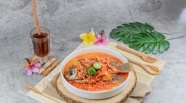 Seporsi seblak kuah pedas mengepul yang menggoda selera, dengan berbagai topping melimpah seperti bakso, sosis, dan ceker ayam, siap dinikmati. Hidangan ini memancarkan warna merah merona dari cabai dan aroma khas kencur yang menggugah selera para pencinta makanan pedas.