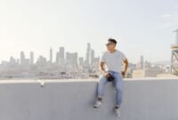 Seorang profesional urban melakukan meditasi di atap gedung pencakar langit, merefleksikan tren kaum urban 2026 yang mencari ketenangan di tengah hiruk-pikuk kota. Pemandangan ini menyoroti bagaimana individu menciptakan ruang personal untuk keseimbangan mental di lingkungan perkotaan yang dinamis.
