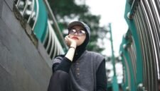 Seorang pemuda bergaya kasual dengan jaket denim dan kaus grafis dari distro lokal, menunjukkan semangat berbusana yang unik dan otentik di tengah keramaian kota. Pilihan gaya ini merefleksikan identitas diri serta dukungan terhadap karya desainer muda Indonesia.
