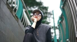 Seorang pemuda bergaya kasual dengan jaket denim dan kaus grafis dari distro lokal, menunjukkan semangat berbusana yang unik dan otentik di tengah keramaian kota. Pilihan gaya ini merefleksikan identitas diri serta dukungan terhadap karya desainer muda Indonesia.