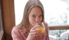 Seorang perempuan muda menikmati segelas jamu kunyit asam di sebuah kafe modern, menunjukkan bagaimana ramuan tradisional ini kini menjadi bagian gaya hidup sehat urban. Racikan herbal ini menawarkan kesegaran dan khasiat alami yang telah diwariskan turun-temurun.