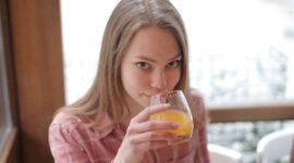 Seorang perempuan muda menikmati segelas jamu kunyit asam di sebuah kafe modern, menunjukkan bagaimana ramuan tradisional ini kini menjadi bagian gaya hidup sehat urban. Racikan herbal ini menawarkan kesegaran dan khasiat alami yang telah diwariskan turun-temurun.