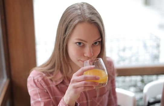 Seorang perempuan muda menikmati segelas jamu kunyit asam di sebuah kafe modern, menunjukkan bagaimana ramuan tradisional ini kini menjadi bagian gaya hidup sehat urban. Racikan herbal ini menawarkan kesegaran dan khasiat alami yang telah diwariskan turun-temurun.