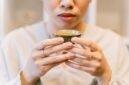 Seorang wanita menikmati segelas jamu kunyit asam yang menyegarkan, menunjukkan perpaduan antara tradisi dan gaya hidup sehat masa kini. Berbagai rempah dan bahan alami, seperti kunyit dan asam jawa, terlihat di sekelilingnya, menggambarkan kekayaan warisan herbal Indonesia.