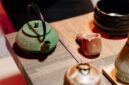 Seorang wanita sedang menyeduh teh hijau dengan cermat, menunjukkan ritual yang tenang dan penuh perhatian dalam mempersiapkan minuman sehat ini. Proses penyeduhan yang tepat sangat penting untuk mengeluarkan seluruh khasiat dan aroma alami dari daun teh hijau berkualitas.