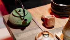 Seorang wanita sedang menyeduh teh hijau dengan cermat, menunjukkan ritual yang tenang dan penuh perhatian dalam mempersiapkan minuman sehat ini. Proses penyeduhan yang tepat sangat penting untuk mengeluarkan seluruh khasiat dan aroma alami dari daun teh hijau berkualitas.