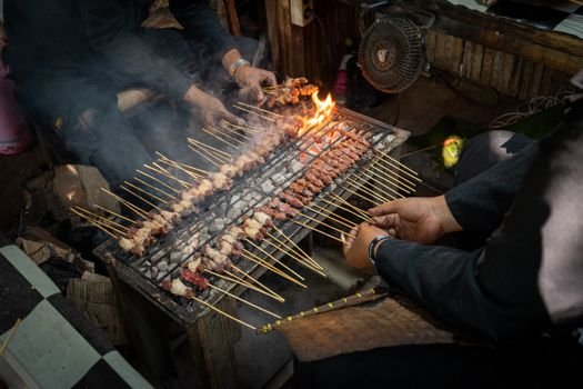 Seorang penjual sedang membuat surabi di atas wajan tanah liat yang dipanaskan menggunakan bara arang, metode tradisional yang memberikan aroma dan cita rasa khas pada kue legendaris ini. Asap tipis yang mengepul menambah nuansa otentik dalam proses pembuatan surabi.