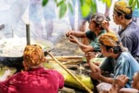 Seorang ibu sedang meracik jamu tradisional dengan bahan-bahan alami segar di dapur, menggambarkan proses otentik pembuatan minuman berkhasiat yang kaya akan rempah khas Indonesia.