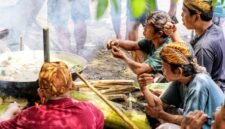 Seorang ibu sedang meracik jamu tradisional dengan bahan-bahan alami segar di dapur, menggambarkan proses otentik pembuatan minuman berkhasiat yang kaya akan rempah khas Indonesia.