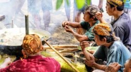 Seorang ibu sedang meracik jamu tradisional dengan bahan-bahan alami segar di dapur, menggambarkan proses otentik pembuatan minuman berkhasiat yang kaya akan rempah khas Indonesia.
