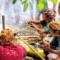 Seorang ibu sedang meracik jamu tradisional dengan bahan-bahan alami segar di dapur, menggambarkan proses otentik pembuatan minuman berkhasiat yang kaya akan rempah khas Indonesia.