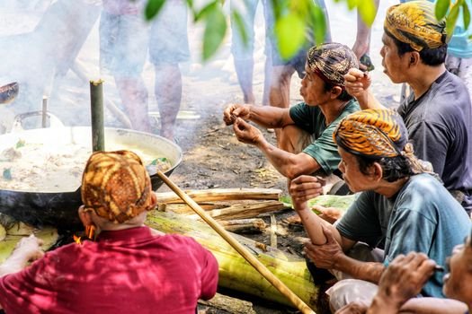 Seorang ibu sedang meracik jamu tradisional dengan bahan-bahan alami segar di dapur, menggambarkan proses otentik pembuatan minuman berkhasiat yang kaya akan rempah khas Indonesia.